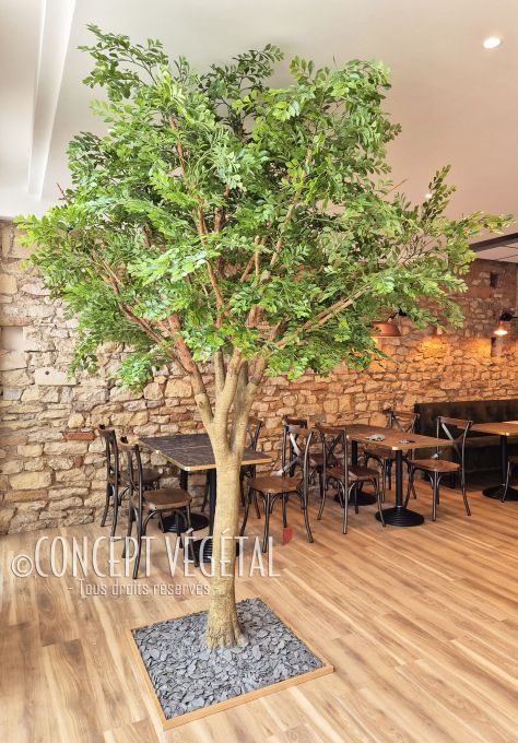 Grand Arbre artificiel vert avec tronc naturel planté au sol avec surfaçage ardoise au milieu d'un restaurant