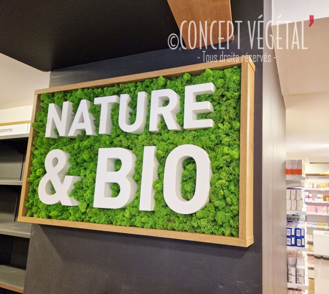 tableau végétal en mousse vert clair avec un logo nature & bio dans une pharmacie . le cadre est en bois clair 