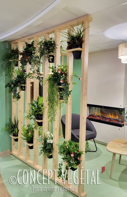 Plantes artificielles en pot placés dans une structure séparative en bois à côté d'un salon d'attente pourvu d'un fauteuil et d'une cheminée à l'éthanol